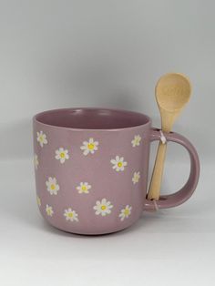 a pink mug with white daisies on it and a wooden spoon in the cup