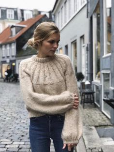 a woman is standing on the street with her hand in her pocket and wearing a sweater