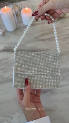 a woman holding a white beaded purse with pearls on the handle and chain attached to it