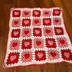 a red and white crocheted afghan with hearts on the front, sitting on a wooden floor