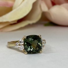 a close up of a ring with a green stone and diamonds on the side next to a flower