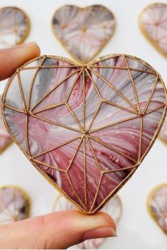 a hand holding a heart shaped decoration in front of hearts on a white background with gold wire