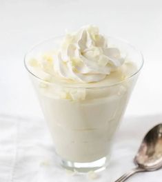 a glass bowl filled with whipped cream next to two spoons on a white surface