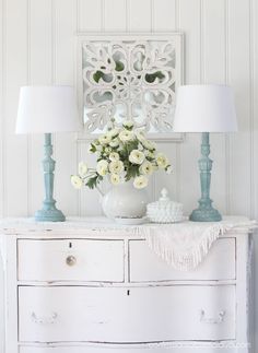 a white dresser with flowers and two lamps on top