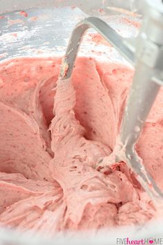 a mixer filled with pink frosting sitting on top of a counter