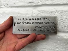 a hand holding a metal plaque that says as iron sharpens 1011, so one person sharpening another