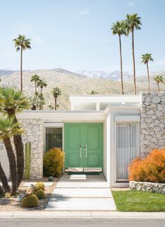 a green door in front of a house with palm trees and mountains in the background