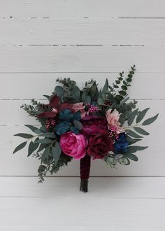 a bridal bouquet with purple and red flowers on a white wooden background in front of wood planks