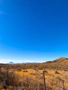 an open field with mountains in the distance and blue skies above it on a sunny day