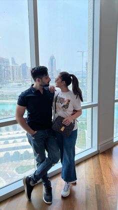 a man and woman standing next to each other in front of a window looking out at the city