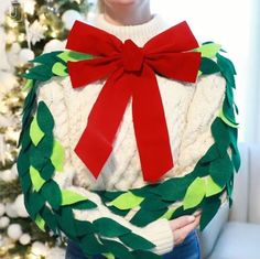 a woman wearing a sweater with a christmas wreath on it and a red bow around her neck