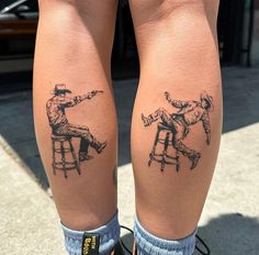 two people sitting on stools with tattoos on their legs, one is pointing at the other