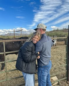 a man and woman standing next to each other in front of a fence with horses