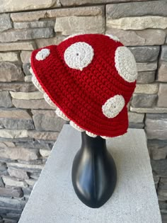 a red and white crocheted mushroom hat sitting on top of a black mannequin head