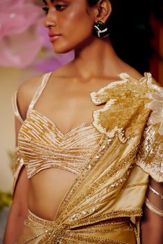 The flower patch on the shoulder seems like it is blooming from the joy of the season. The draped saree made with lightweight fabric materializes the concept of a fairy. The gold saree is embellished with beadwork and applique flowers all around to appear as if standing amongst flowers. Cold shoulder style blouse with back hook Pre-draped saree with a flower patch on the shoulder accentuated with beads and sequins embroidery. Metal zip on the saree. From Moledro’s Taabir collection. DELIVERY TIM Festive Gold Embellished Pre-draped Saree, Embellished Raw Silk Saree, Gold Embellished Tissue Silk Saree, Gold Embellished Choli, Festive Gold Pre-draped Saree With Sequins, Embellished Gold Choli, Glamorous Gold Dupatta Traditional Drape, Glamorous Gold Blouse Piece With Dupatta, Glamorous Silk Pre-draped Saree With Sheer Dupatta