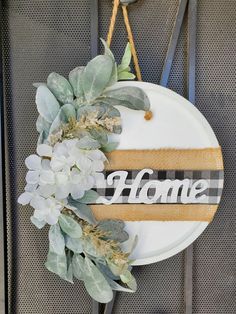 a sign that says home hanging on a wall next to some flowers and plants in front of it