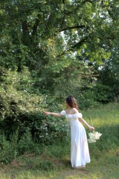 a woman in a white dress is holding her arms out and looking at the trees