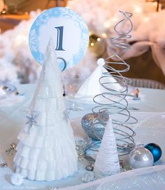 a table topped with white christmas trees next to blue and silver ornaments on top of a table