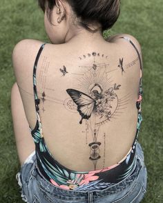 a woman sitting on the grass with her back to the camera and tattoos on her body