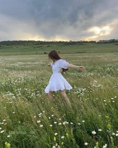 a girl in a white dress walking through tall grass