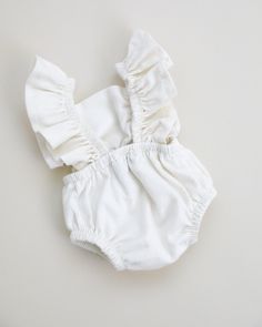 a white baby romper with ruffles on the front and bottom, sitting on top of a table