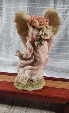 an angel figurine holding a bouquet of flowers on top of a wooden table