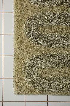 a bathroom rug on the floor in front of a tiled wall