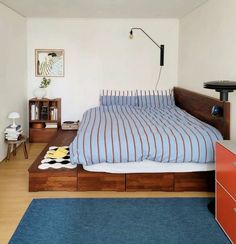 a bed sitting in a bedroom next to a blue rug and wooden dresser under a lamp