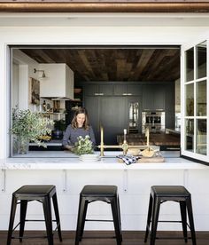 a woman sitting at a kitchen counter with three stools in front of the window