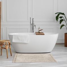 a white bathtub sitting on top of a wooden floor next to a chair and potted plant