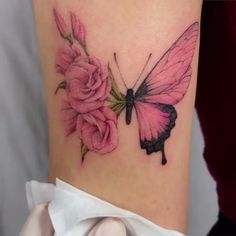 a pink butterfly on the back of a woman's thigh with roses around it