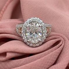 an oval cut diamond ring on top of pink fabric with diamonds around the shants