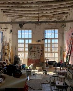 an artist's studio with lots of clutter on the floor and windows in the background