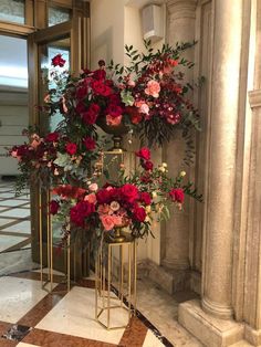 a tall vase with red and pink flowers sitting on top of a gold stand in front of a doorway