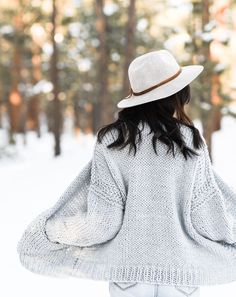 a woman wearing a white hat and sweater is standing in the snow with her back to the camera