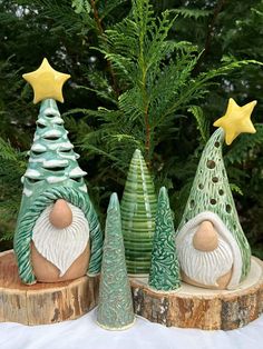 three ceramic christmas trees sitting next to each other on top of a tree stump in front of a pine tree