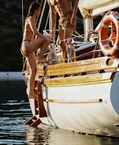 a man and woman standing on the deck of a sailboat in the water next to each other