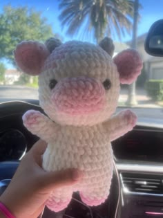 a hand holding a small stuffed animal in the dashboard of a car with palm trees behind it