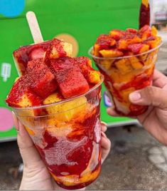 two people holding up glasses filled with fruit and ice cream on top of each other