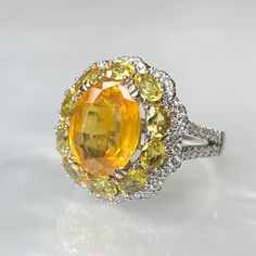 A pleasing eye-catching oval shaped orange-yellow sapphire cocktail ring featuring a 3.89 carat center stone surrounded by 2.13 carats of smaller oval yellow sapphires and with 0.57 carats of diamonds. *Complimentary resizing is available up to 3 sizes larger or smaller than stated size. WEB ID: R672 Yellow Sapphire Engagement Ring, Dainty Earrings Studs, Yellow Sapphire Ring Engagement, Antique Emerald Ring, Engagement Ring Sapphire, Engagement Ring Gemstone, Yellow Sapphire Ring, Vintage Sapphire Ring, Sapphire Cocktail Ring