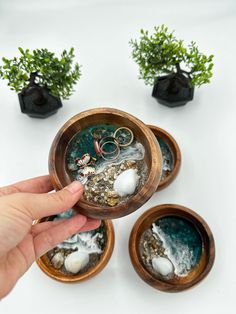 a person is holding their hand over some small pots with plants in them on a white surface