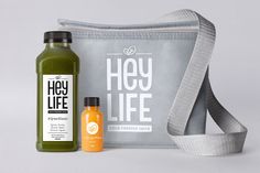 two bottles of juice next to a bag on a white surface with the words hey life printed on it