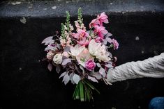 a bouquet of pink and white flowers is being held by someone's hand on the ground