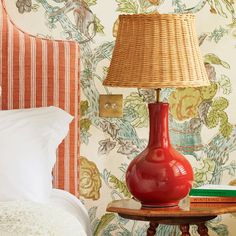 a red lamp sitting on top of a table next to a bed