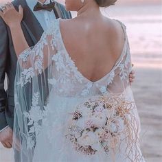 a bride and groom standing on the beach at sunset with their arms around each other