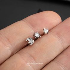 a person's hand holding two small silver studs with white pearls on them