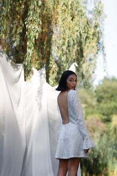 a woman in a short white dress standing next to a tree with her back turned