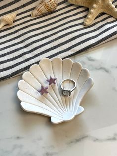 a ring sits on a shell shaped dish next to starfish and seashells