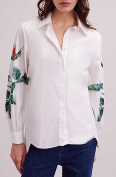 a woman is wearing a white shirt with roses on the sleeves and cuffs, while she has her hands in her pockets