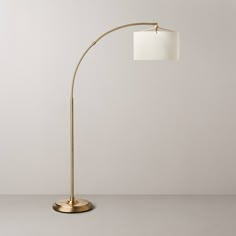 a gold floor lamp with a white shade on the base and a round light fixture